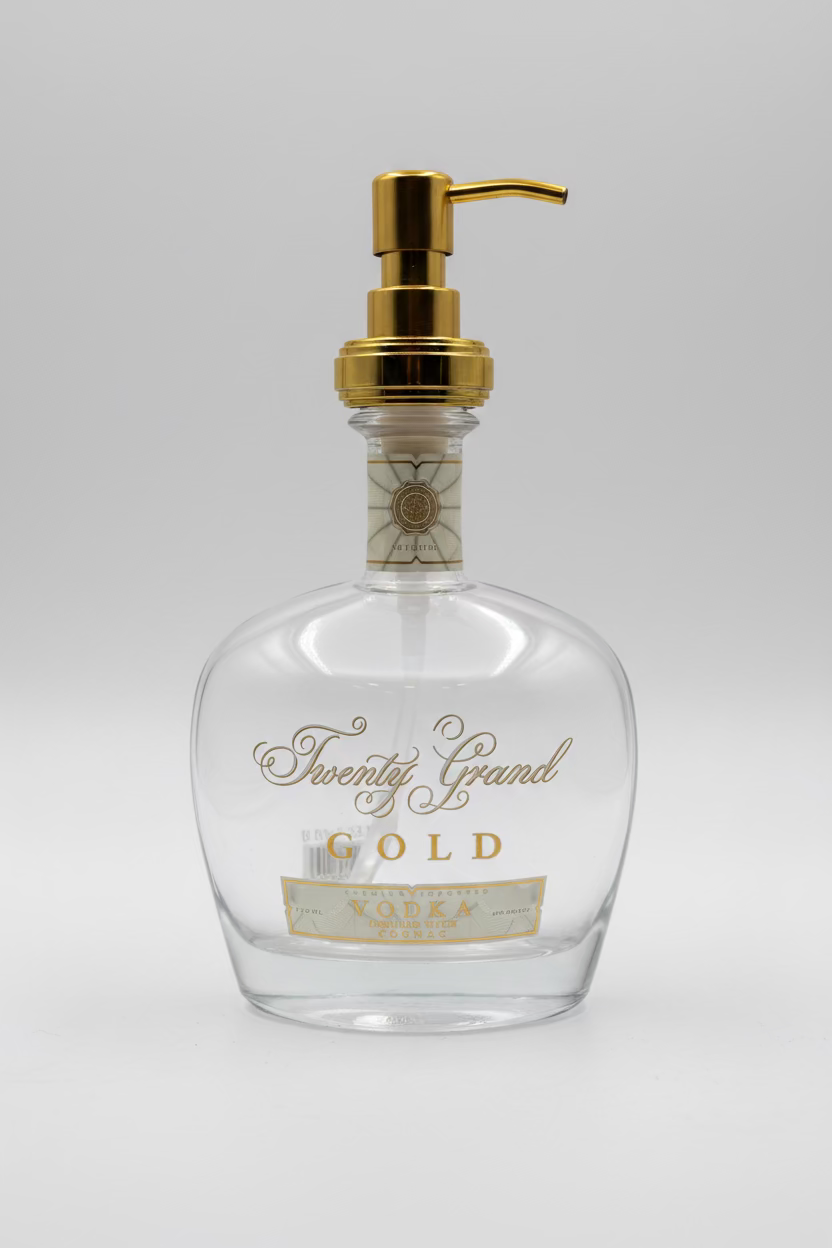 A clear glass bottle of Gold Vodka with a gold-colored cap and a pump dispenser, standing on a table with a floral arrangement in the background.