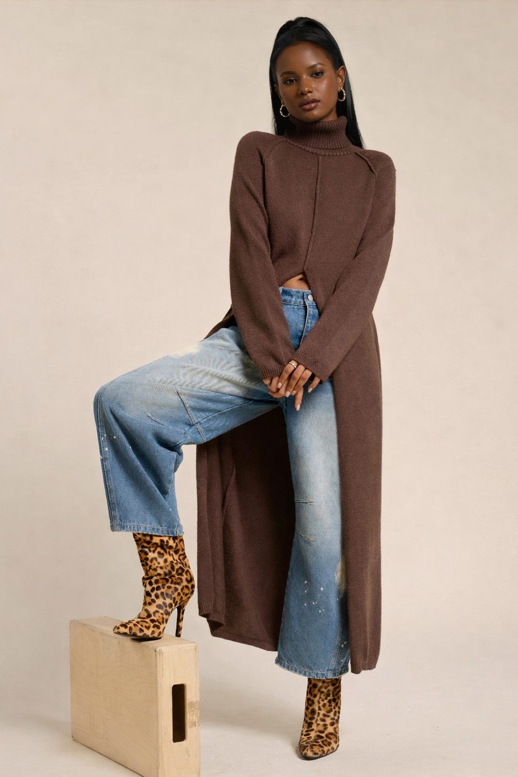 Woman wearing a long brown sweater, blue jeans, and leopard print boots on a beige background